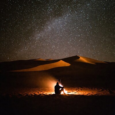 Man by campfire under starry desert sky