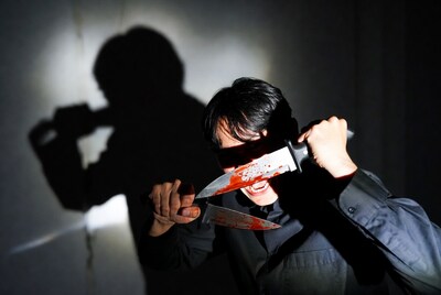 Man holding bloody knife across face