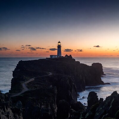 Lighthouse on rocky cliff at sunset
