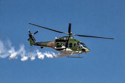Green military helicopter flying with smoke trails