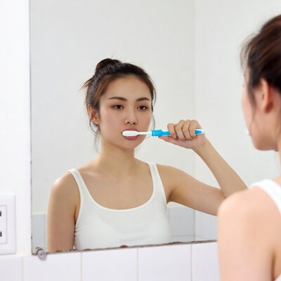 Asian woman brushing teeth in mirror