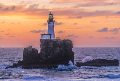 Lighthouse on rocky island at sunset