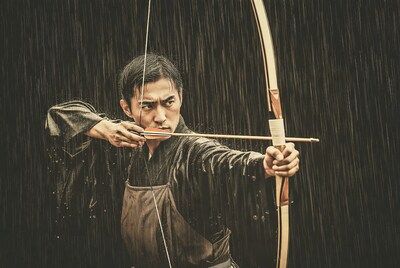 Asian man shooting bow in rain