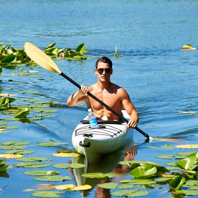 Shirtless man kayaking through lily pads