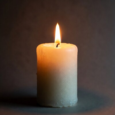 Burning white candle on dark background