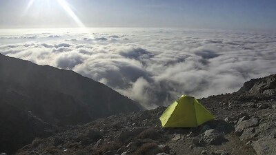 Green tent on mountain above clouds