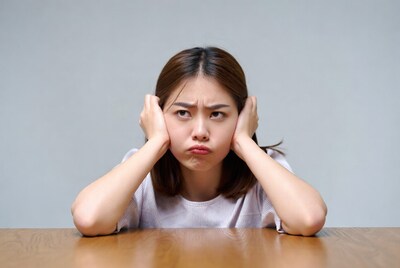 Asian woman covering ears at table