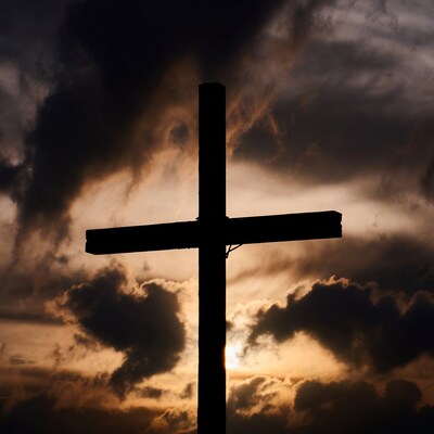 Silhouette cross against stormy sunset sky