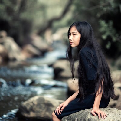Asian girl sitting by forest stream
