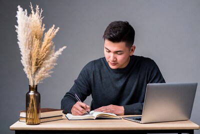 Asian man writing in notebook at desk