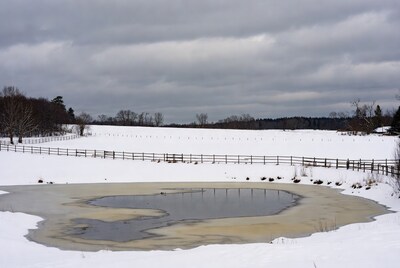 Snowy field with melting pond and fence