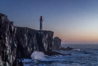 White lighthouse on rocky cliffs at sunset