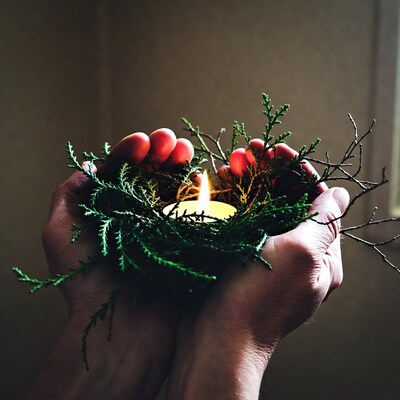 Hands holding candle in evergreen wreath