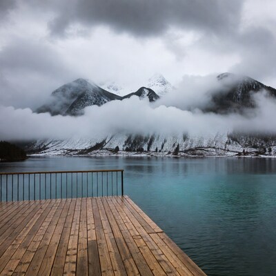 Wooden pier over misty lake with snowy mountains