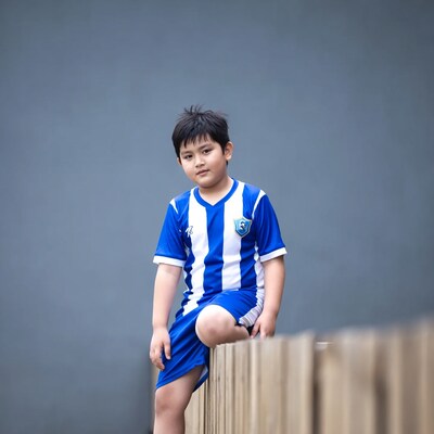 Asian boy in blue soccer jersey on fence