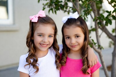 Twin girls with bows smiling outdoors