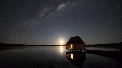 Lit cabin on lake under Milky Way