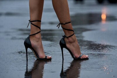 Woman's black strappy stilettos on wet pavement