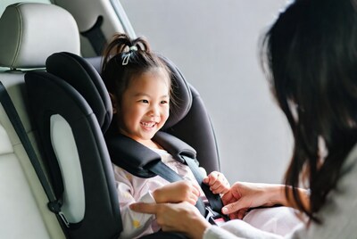 Asian mother buckling toddler girl in car seat