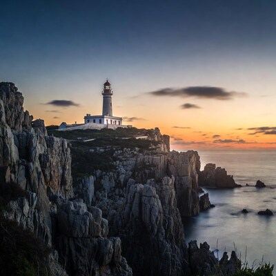 Lighthouse on rocky cliffs at sunset