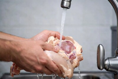 Man washing raw chicken under faucet