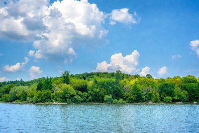 Lake with forested hillside under blue sky