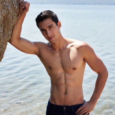 Shirtless muscular man leaning on rock by lake