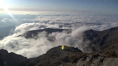Yellow tent on mountain above clouds