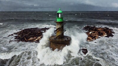 Green lighthouse amid crashing waves and driftwood