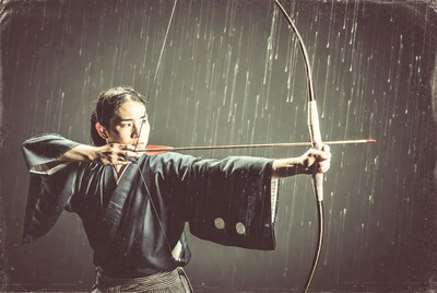 Asian man shooting bow in rain