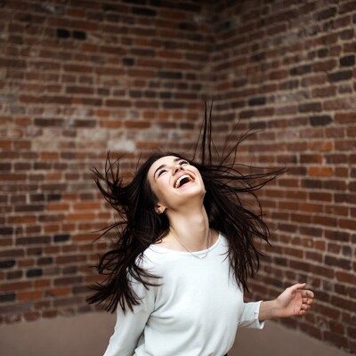 Woman laughing with hair flying against brick wall