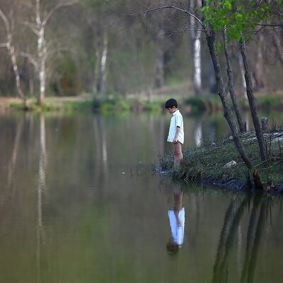 Boy standing by lake with reflection