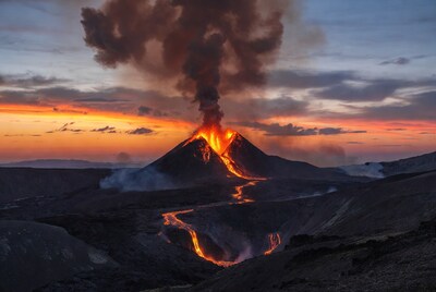 Erupting volcano at sunset with lava flows
