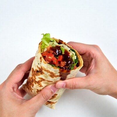 Hands holding open wrap with tomatoes lettuce