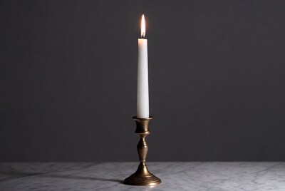 Lit white candle on brass candlestick