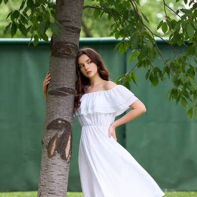 Woman leaning against tree in white dress