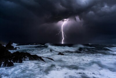 Lightning striking ocean over rocky coast