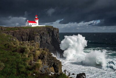 White lighthouse on cliff with crashing waves