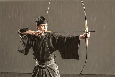 Asian man shooting Japanese bow in rain