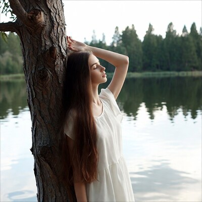 Woman leaning against tree by lake