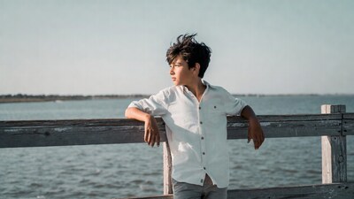 Boy leaning on pier railing by sea