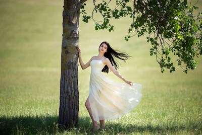 Woman in white dress by tree in grass