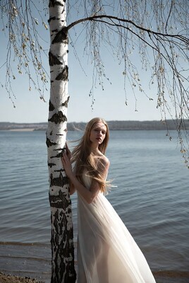 Blonde woman leaning on birch tree by lake