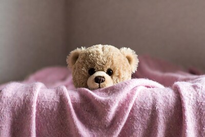 Teddy bear peeking from pink blanket