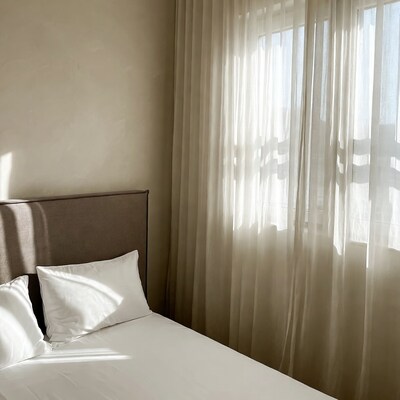 Cozy bed with pillows by sheer curtains