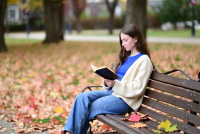 Young woman reading book on park bench