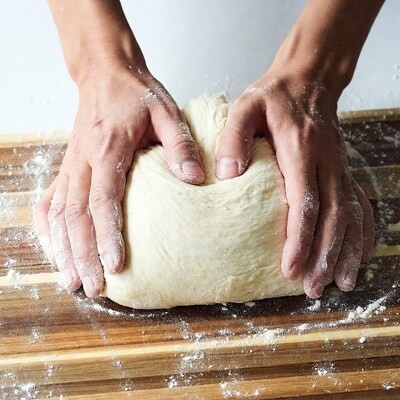 Hands kneading dough on wooden board