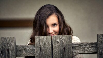 Young woman peeking over wooden fence