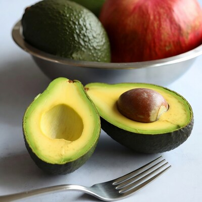 Avocado halves with fork and fruit bowl
