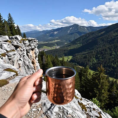 Hand holding copper mug on mountain peak